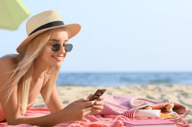 Deniz sahilinde cep telefonu kullanan güzel genç bir kadın.