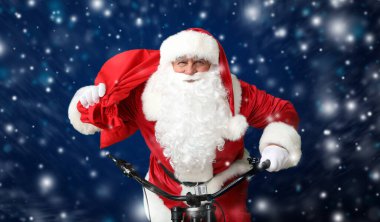 Çantalı Noel Baba koyu renk arka planda bisiklet sürüyor.