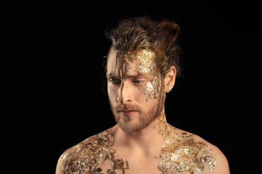 Siyah arka planda altın rengi boyası olan yakışıklı bir genç.