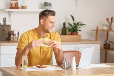 Evde laptopla lezzetli quesadilla yiyen yakışıklı genç adam.