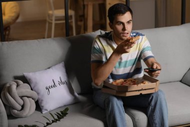 Yakışıklı genç adam akşam evde TV izlerken lezzetli pizza yiyor.