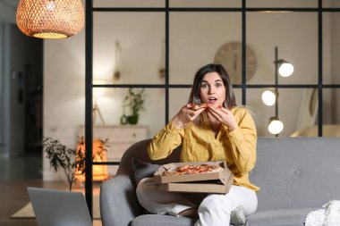 Şaşırmış genç bir kadın akşam evde lezzetli pizzalar yiyor.