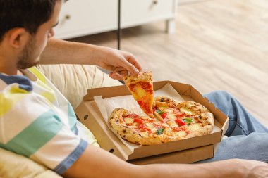 Yakışıklı genç adam evde lezzetli pizzalar yiyor.