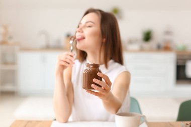 Evde lezzetli çikolata ezmesi yiyen güzel genç bir kadın.