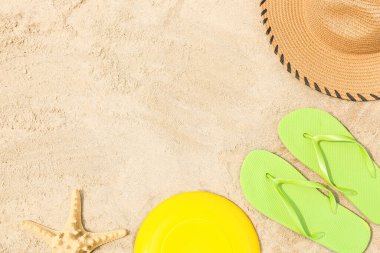 Frizbi diski, şapka, parmak arası terlik ve kumdaki denizyıldızı.