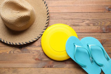 Tahta arka planda frizbi diski, şapka ve parmak arası terlikler