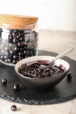 Kavanoz ve kase, arka planda siyah frenk üzümü reçeli.