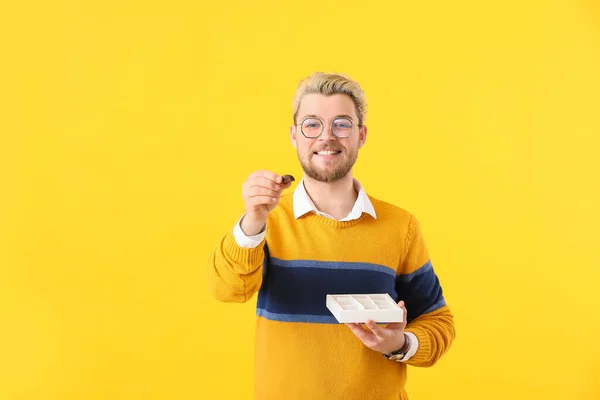 Schöner Junger Mann Mit Schachtel Schokoladenbonbons Auf Farbigem Hintergrund — Stockfoto