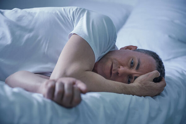 Депрессивный зрелый мужчина лежит на кровати