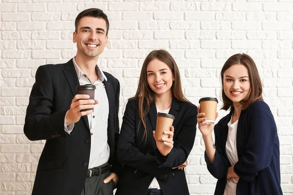Business colleagues drinking coffee near brick wall