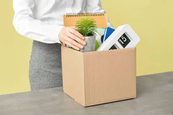 Fired female worker with personal things on table against color background