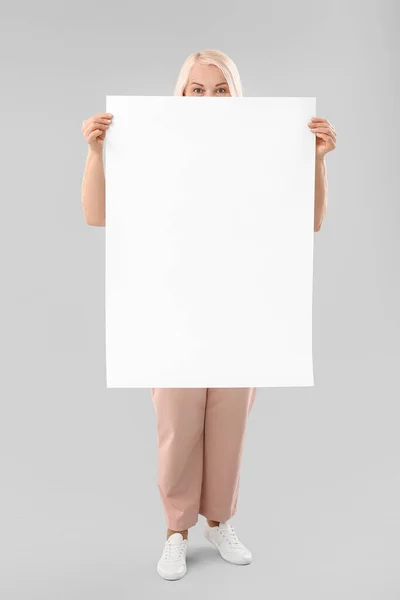 Mature woman with blank poster on light background