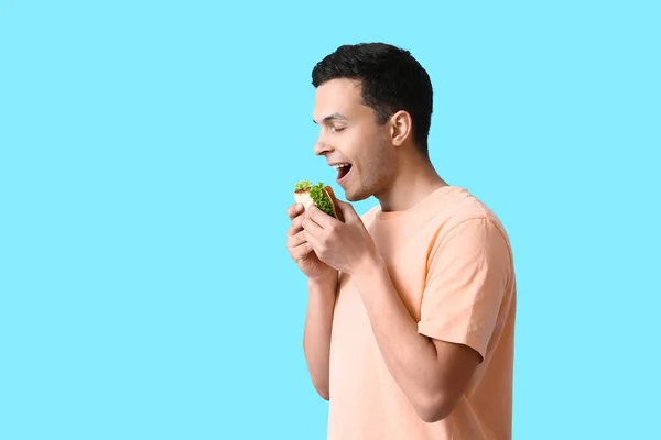 Молодой Человек Ест Вкусный Сэндвич Цветном Фоне — стоковое фото