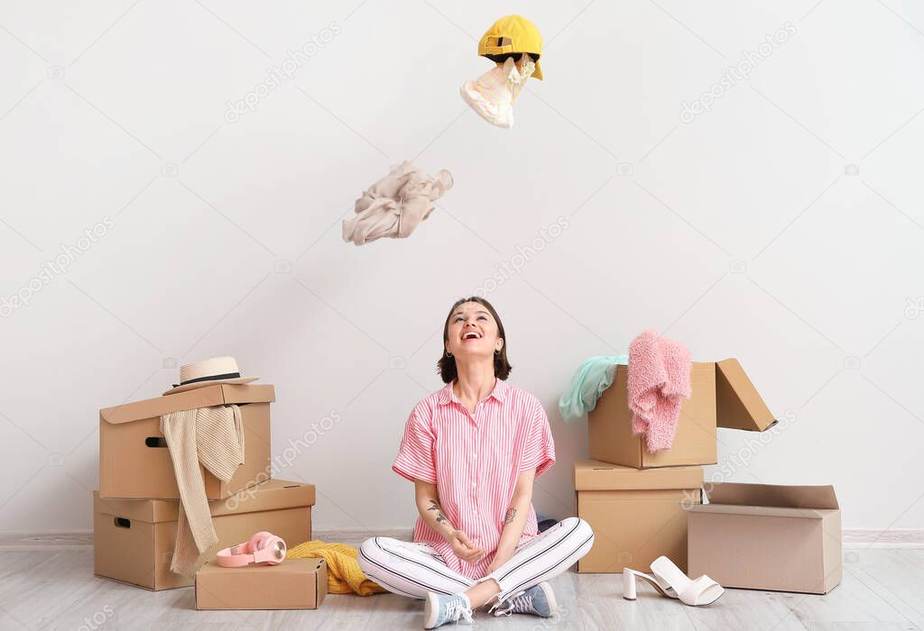 Young woman with clothes and wardrobe boxes near light wall