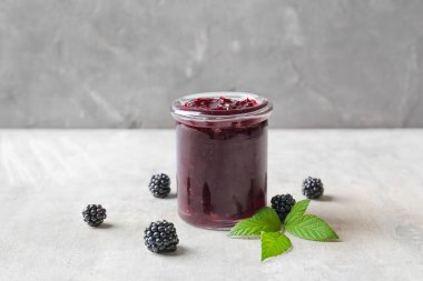 Gri arka planda lezzetli böğürtlen reçeli kavanozu