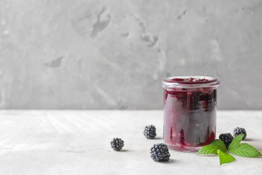 Gri arka planda lezzetli böğürtlen reçeli kavanozu