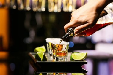 Barmen bardaki masada bardaklara lezzetli tekila dolduruyor.