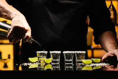 Barmen bardaki masada bardaklara lezzetli tekila dolduruyor.
