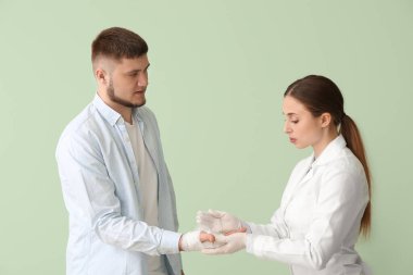 Doktor, arka planda genç bir adamın eline bandaj yapıştırıyor.