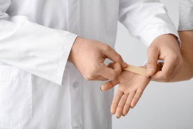 Doktor, arka planda genç bir kadının avucuna sıva yapıştırıyor.