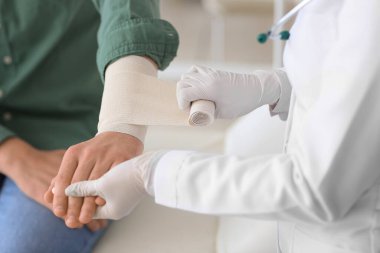 Doktor klinikteki genç adamın koluna bandaj yapıştırıyor.