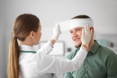 Doktor, klinikteki genç adamın kafasına bandaj yapıştırıyor.
