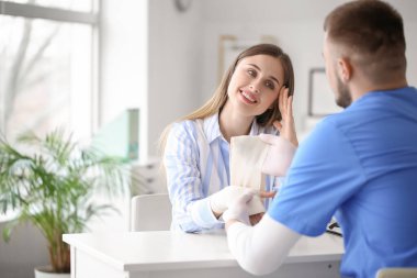 Doktor klinikteki genç bir kadının eline bandaj yapıştırıyor.