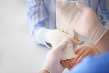 Klinikteki genç bir kadının bileğine bandaj yapıştıran doktor.