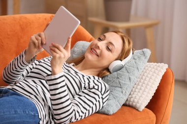 Tabletli olgun bir kadın evde sesli kitap dinliyor.
