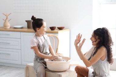 Annesiyle küçük bir kız evde seramik demlik yapıyor.