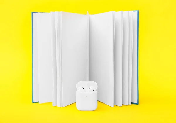 Modern earphones with book on color background