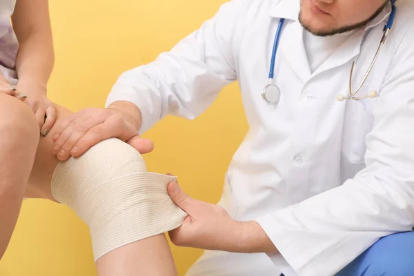 Médico Aplicando Bandagem Joelho Mulher Jovem Fundo Cor — Fotografia de Stock