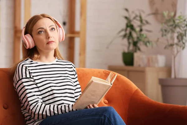 Ώριμη Γυναίκα Ακουστικά Ανάγνωση Βιβλίο Στο Σπίτι — Φωτογραφία Αρχείου