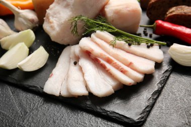 Koyu arkaplanda tuzlanmış domuz yağı dilimleri olan tahta, yakın plan.