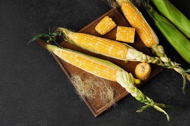 Koyu arkaplanda taze mısır koçanları olan ahşap tahta.