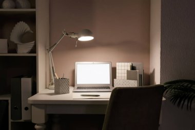 Dizüstü bilgisayarı ve ışık duvarının yanında parlayan lambası olan modern işyeri