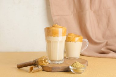 Bardak ve bir fincan lezzetli dalgona hojicha latte, masada pudra var.