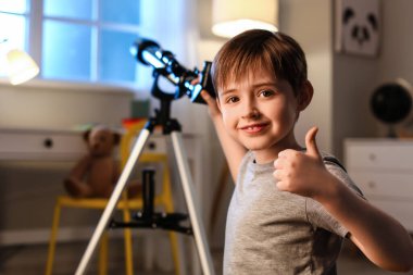 Küçük çocuk akşamları teleskopla yıldızlara bakarken baş parmağını kaldırıyor.