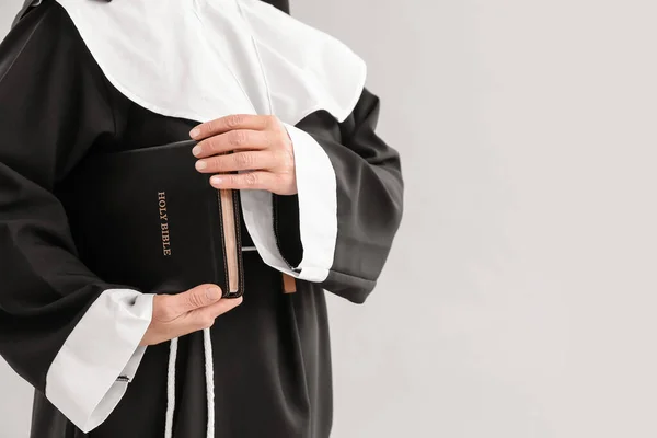 Mature nun with Holy Bible on light background