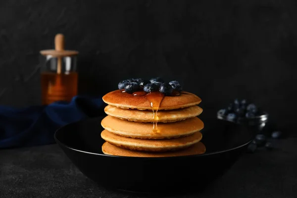 Bowl of tasty pancakes with honey and berries on dark background