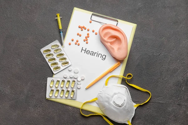 Clipboard with word HEARING, pills and medical mask on dark background