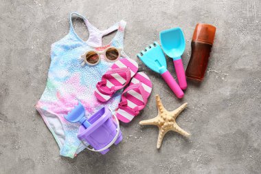 Çocuklar için plaj aksesuarları, şık bir mayo ve grunge arka planda bir şişe güneş kremi.