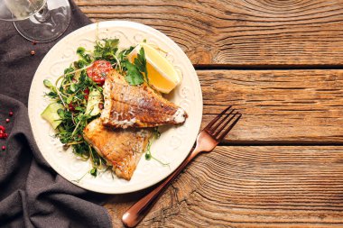 Lezzetli kızarmış balık filetosu ve ahşap arka planda sebze tabağı.