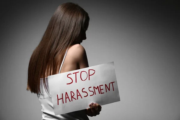 Νεαρή Γυναίκα Κρατώντας Χαρτί Κείμενο Stop Harassment Γκρι Φόντο — Φωτογραφία Αρχείου