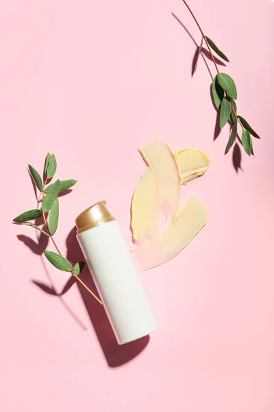 Sample of makeup foundation with bottle of cosmetic product and eucalyptus branches on color background