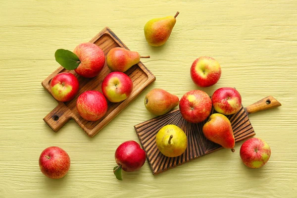 Wooden boards with ripe pears and apples on color background