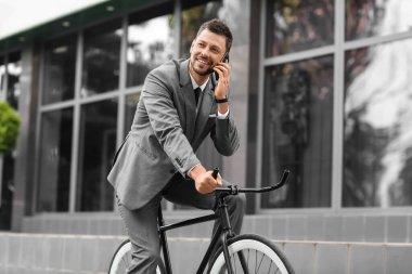 Şehir caddesinde cep telefonu bisikleti süren bir iş adamı.