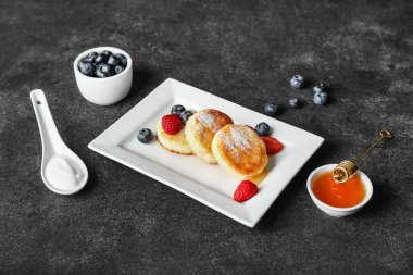 Koyu arkaplanda lezzetli süzme peynirli krep, böğürtlen ve bal tabağı.