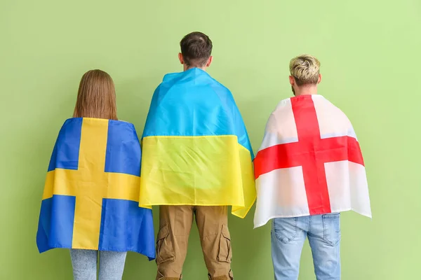 Young people with different flags on color background, back view