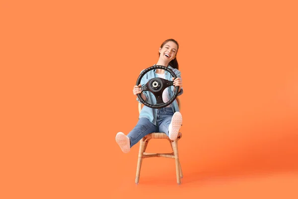 オレンジの背景にステアリングホイールを持つ若い女性 — ストック写真